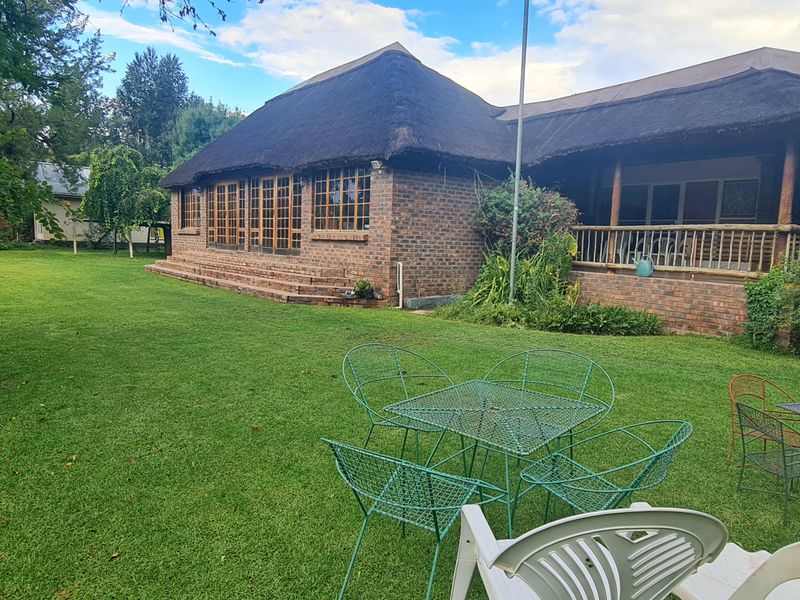 Rear view of a face brick house featuring a traditional thatched roof and a covered patio overlooking a spacious garden.