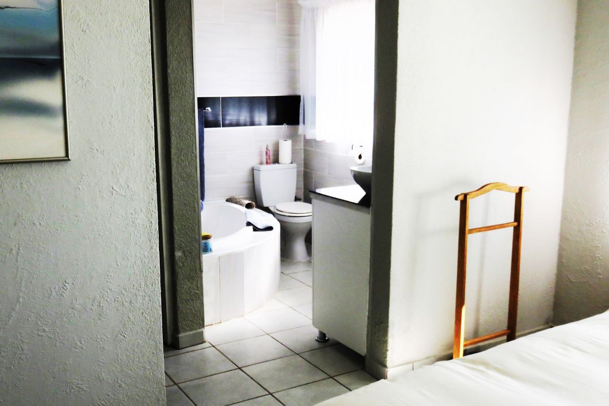 An en-suite bathroom featuring a corner bathtub, a vanity with a basin, and tiled flooring, viewed from the adjacent bedroom.