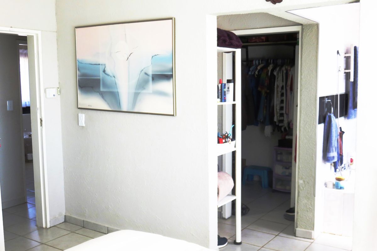 A bedroom interior featuring a walk-in closet area and tiled flooring, providing functional storage space and access to adjacent rooms.