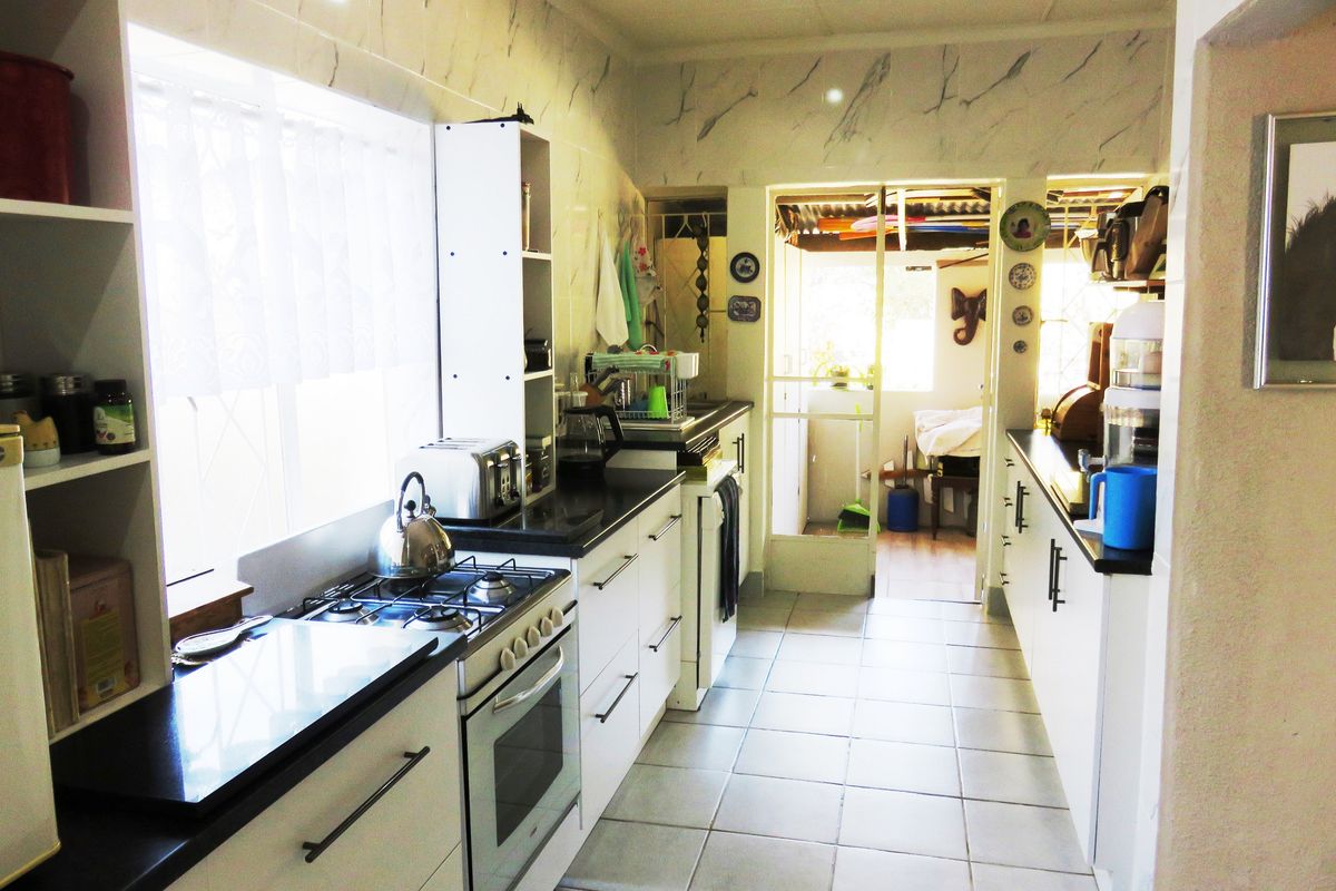 A functional galley-style kitchen featuring white cabinetry, dark countertops, a built-in gas hob and oven, and tiled flooring with direct access to an adjacent area.