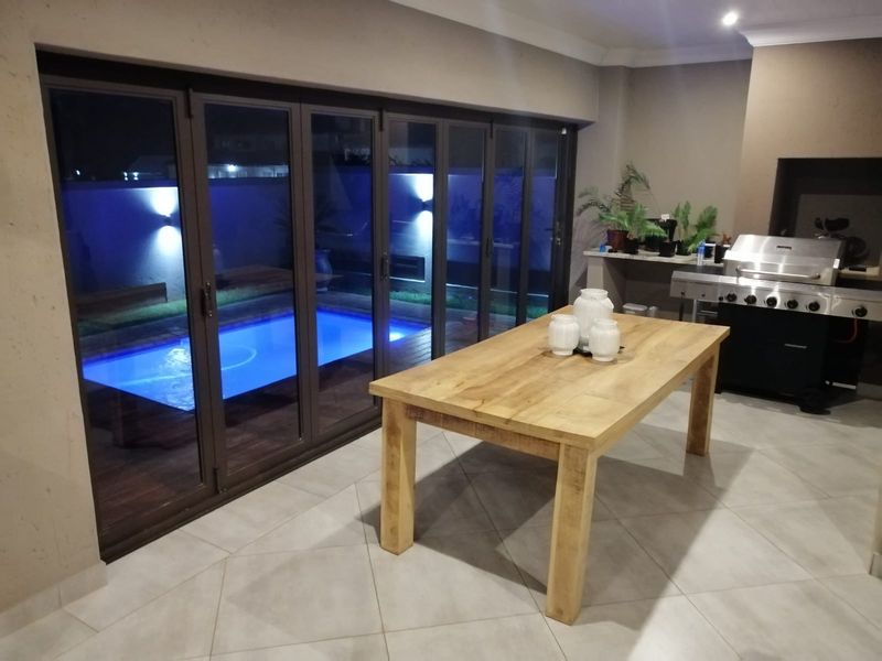 Covered patio area featuring a built-in braai, stone prep counter, and large stacking doors opening onto a pool deck.