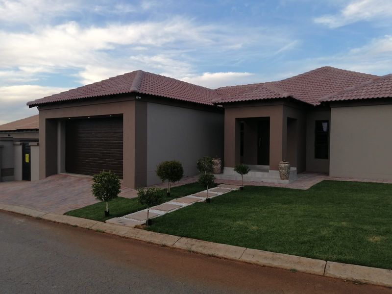 Modern single-story residential home featuring a tiled roof, automated garage, paved driveway, and a well-maintained front garden with a paved walkway.
