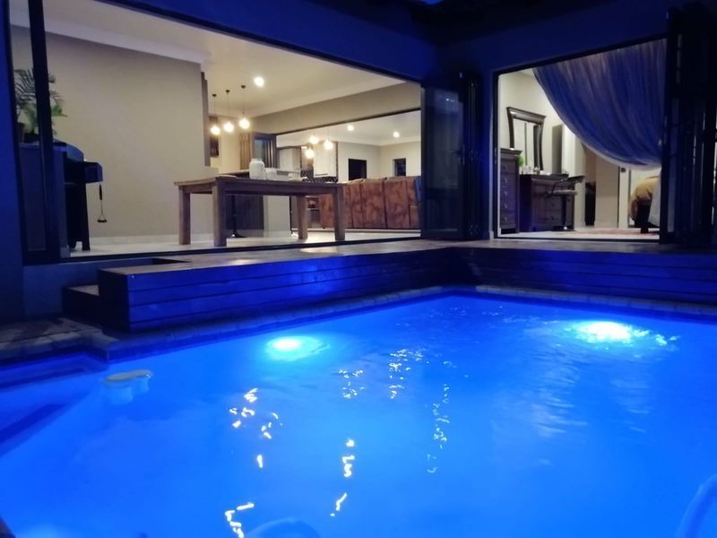 A beautifully illuminated swimming pool area featuring timber decking and large stacking doors that seamlessly connect the outdoor space to the interior living areas.