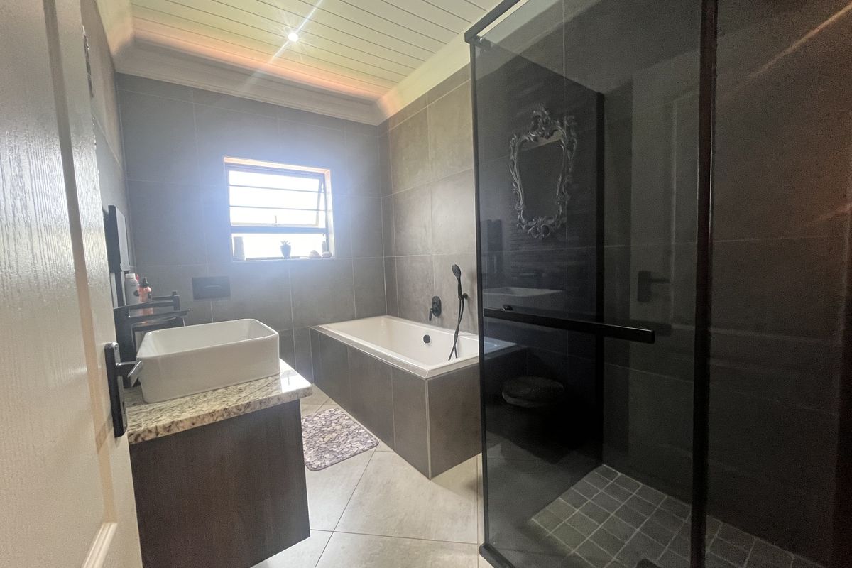 Modern bathroom featuring a built-in bathtub, separate glass-enclosed shower, vessel sink vanity, and neutral floor-to-ceiling tiling with a decorative ceiling finish.