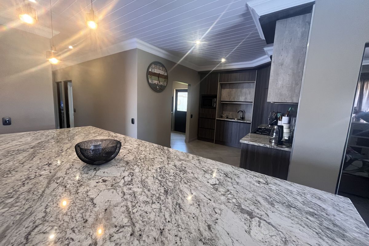 Modern kitchen featuring a large granite island, dark wood cabinetry, built-in appliances, and stylish pendant lighting under a tongue and groove ceiling.