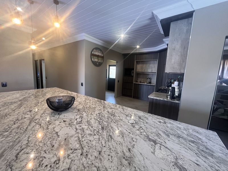 Modern kitchen featuring a large granite island, dark wood cabinetry, built-in appliances, and stylish pendant lighting under a tongue and groove ceiling.