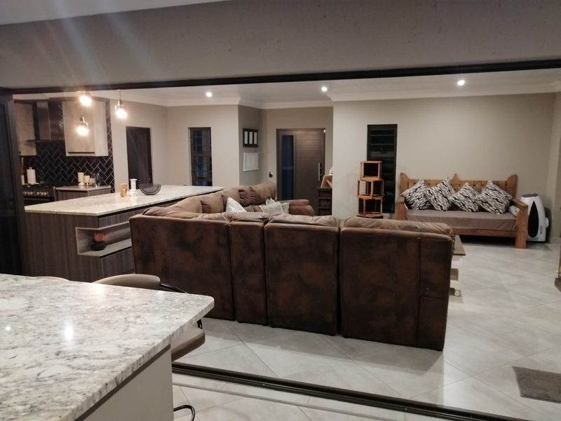Spacious open-plan living area featuring a modern kitchen with stone countertops, a large island, and tiled flooring throughout the connected lounge space.