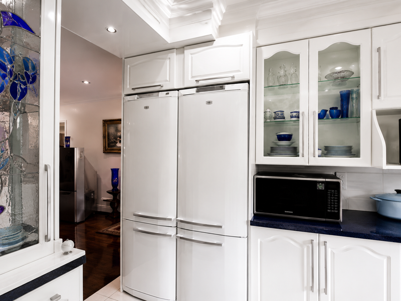 A well-maintained kitchen featuring white cabinetry, integrated refrigeration, built-in microwave, and a decorative stained glass panel, with recessed lighting and crown molding details.