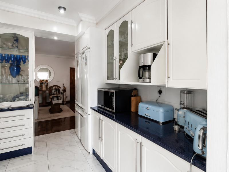 A well-maintained kitchen featuring white cabinetry, dark stone countertops, glass-front display units, and polished marble-look floor tiles.