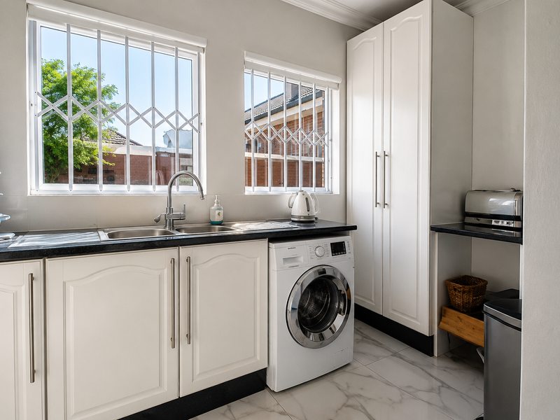 A well-maintained laundry room featuring white built-in cabinetry, a double sink, marble-look floor tiles, and a built-in washing machine.