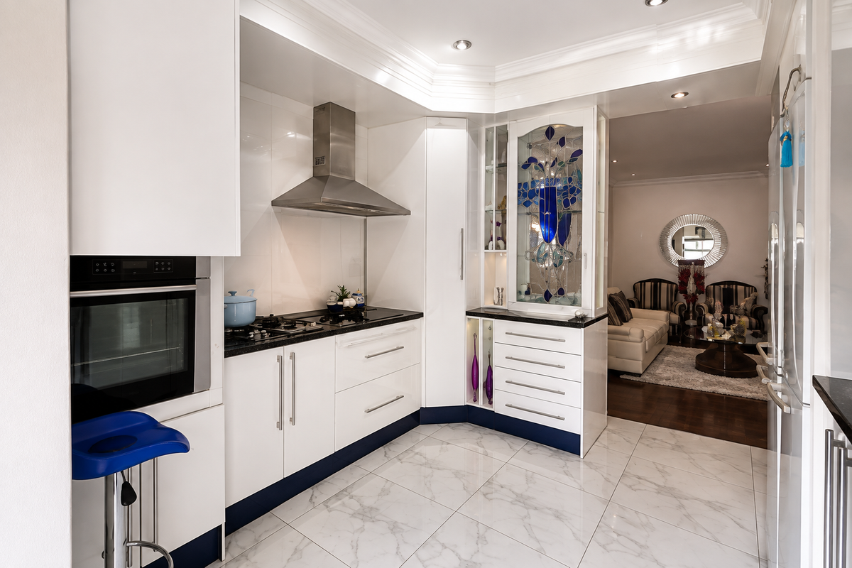 Modern kitchen featuring white cabinetry, granite countertops, built-in oven, gas hob, stainless steel extractor fan, and elegant stained glass display cabinetry.