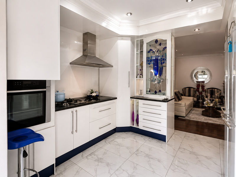 Modern kitchen featuring white cabinetry, granite countertops, built-in oven, gas hob, stainless steel extractor fan, and elegant stained glass display cabinetry.