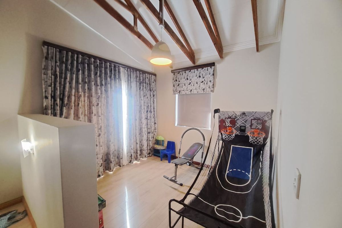 A living area featuring exposed timber rafters, laminate flooring, and a half-height partition wall, offering a bright and versatile space.