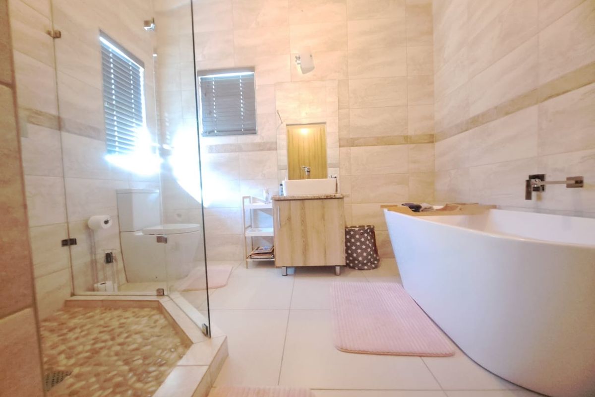 Modern bathroom featuring a freestanding bathtub, glass-enclosed shower with pebble flooring, wall-mounted basin, and neutral floor-to-ceiling tiling.