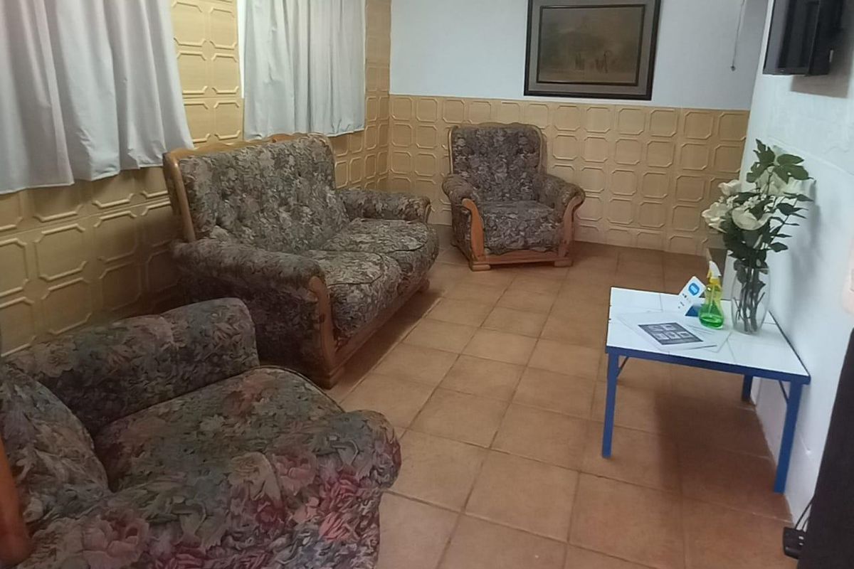 A living room featuring dated textured wall paneling and terracotta-style floor tiles, offering a functional space with potential for modern updates.