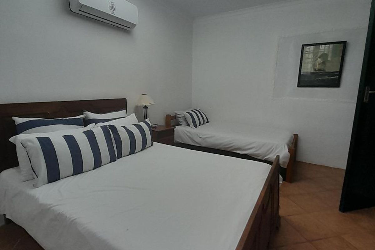 A functional bedroom featuring tiled flooring, a wall-mounted air conditioning unit, and overhead fluorescent lighting.