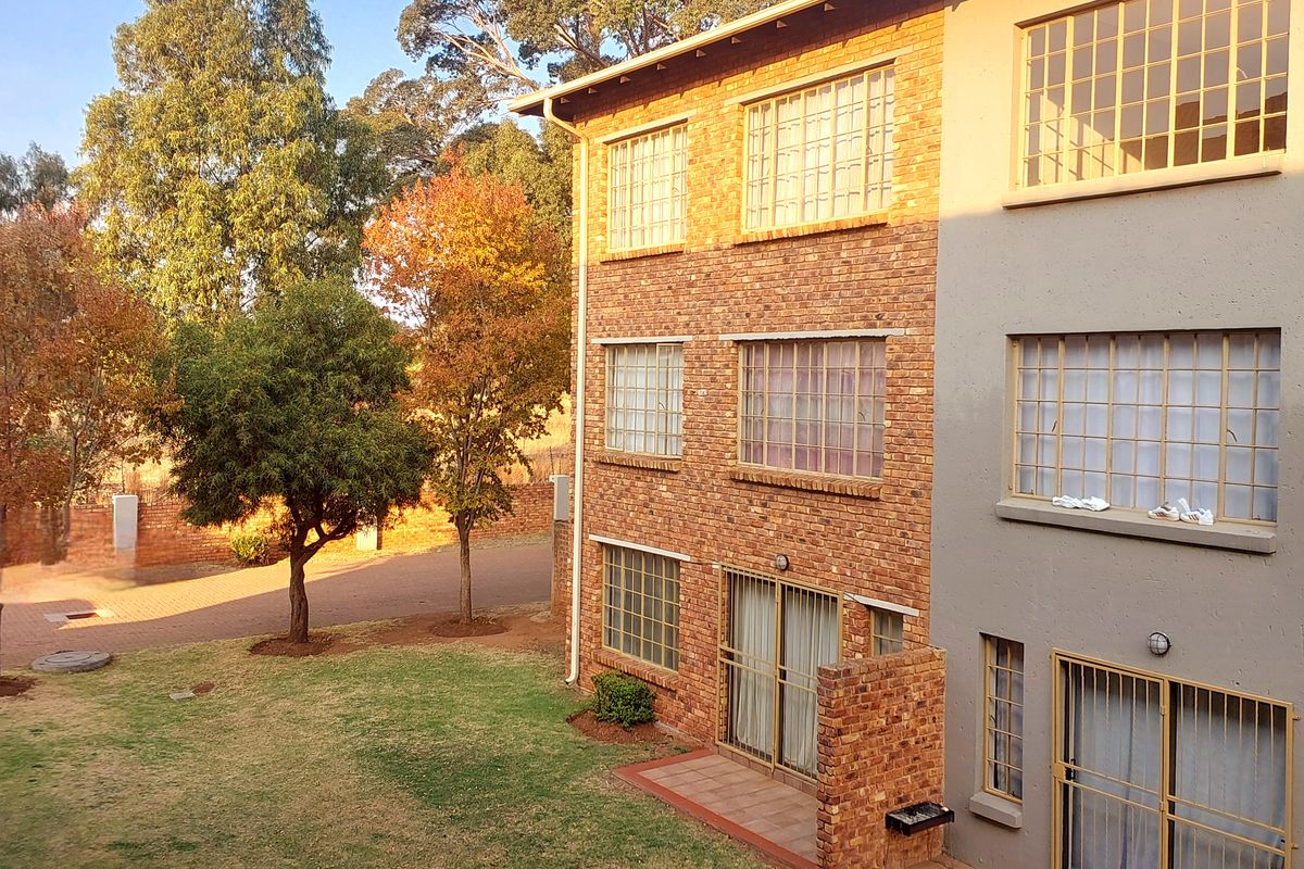 Rear view of a multi-story apartment building featuring brick and rendered facade, ground floor patios, and landscaped garden area.