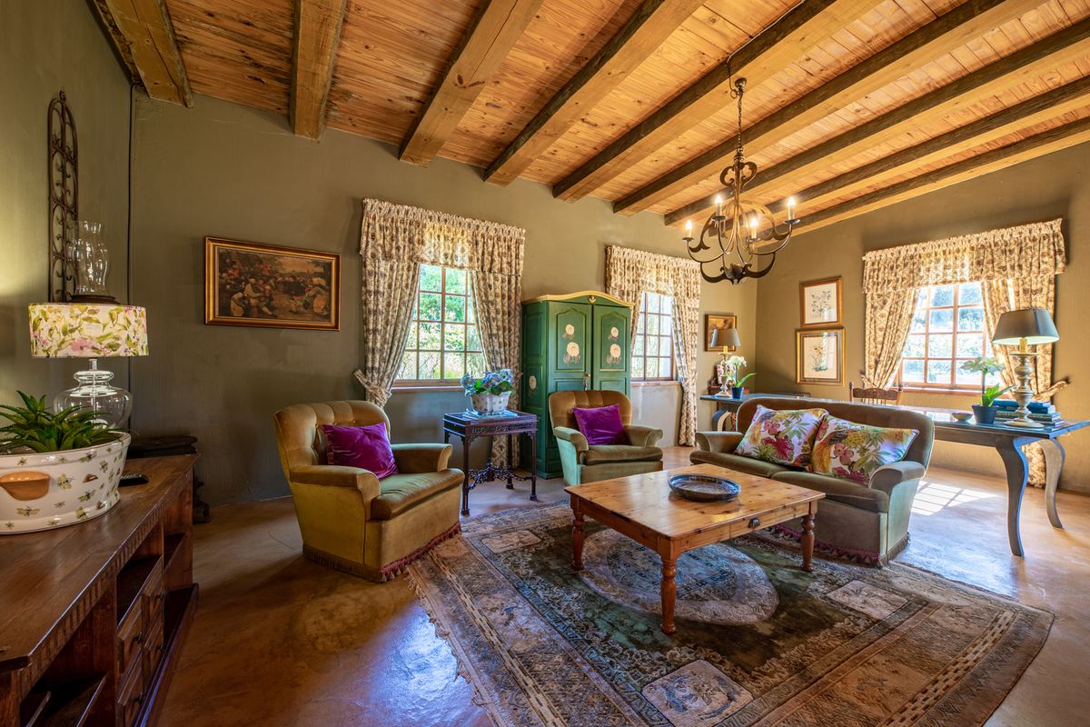 A rustic living room featuring exposed timber ceiling beams, polished concrete floors, and a classic wrought iron chandelier, creating a warm, traditional atmosphere.
