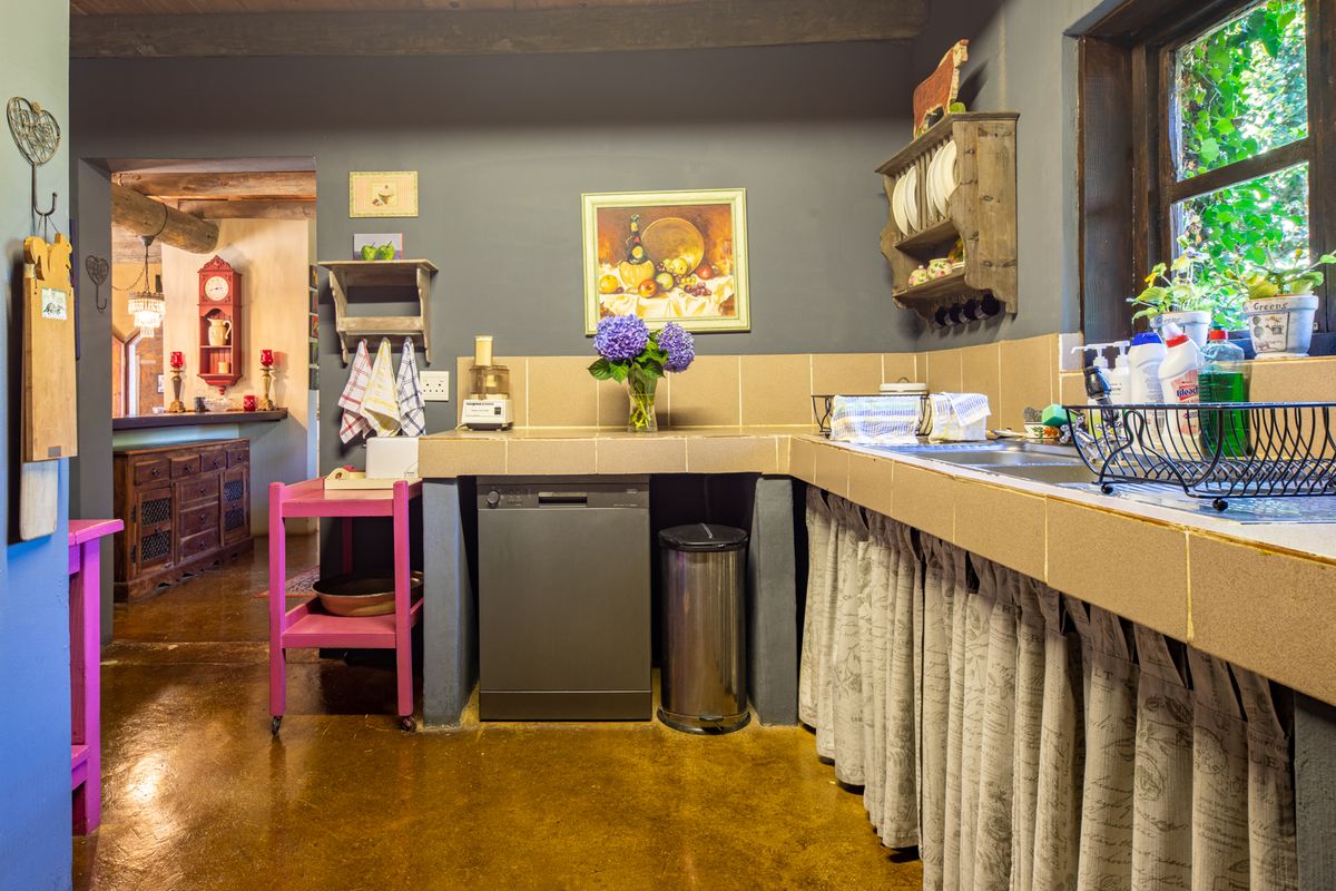 A rustic kitchen featuring tiled countertops, exposed timber ceiling beams, and concrete flooring, offering a warm and traditional farm-style aesthetic.