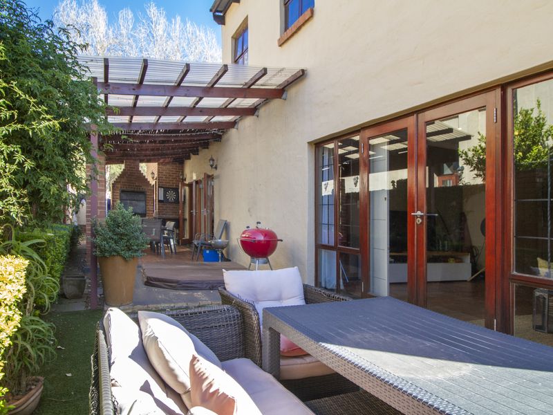 Covered outdoor patio area featuring a built-in brick braai, timber-framed glass doors, and a polycarbonate pergola, providing a functional space for outdoor entertaining.