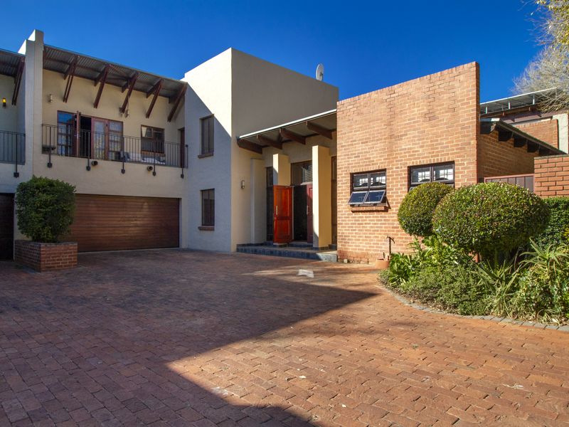 Front elevation of a multi-level house featuring a brick driveway, double garage, and a balcony with a mix of plastered and exposed brick finishes.