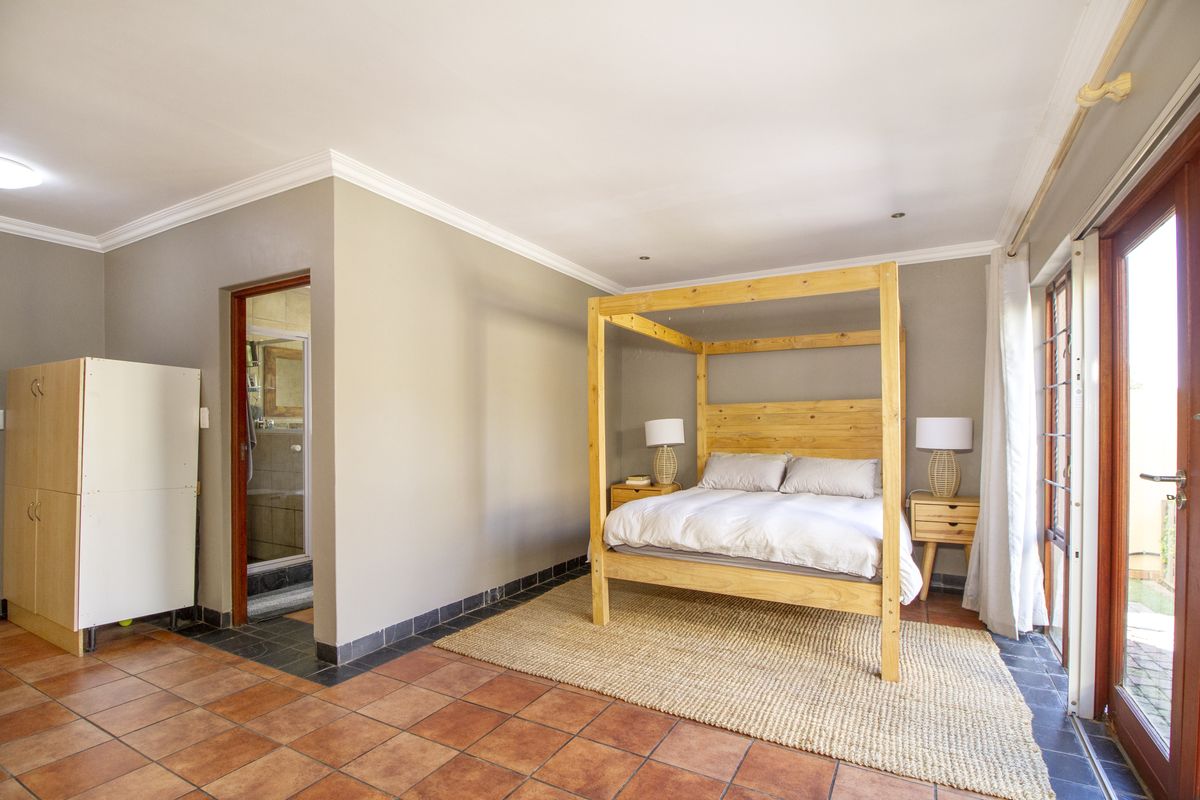 Spacious bedroom featuring terracotta floor tiles, recessed lighting, and direct access to an en-suite bathroom and outdoor area through sliding glass doors.