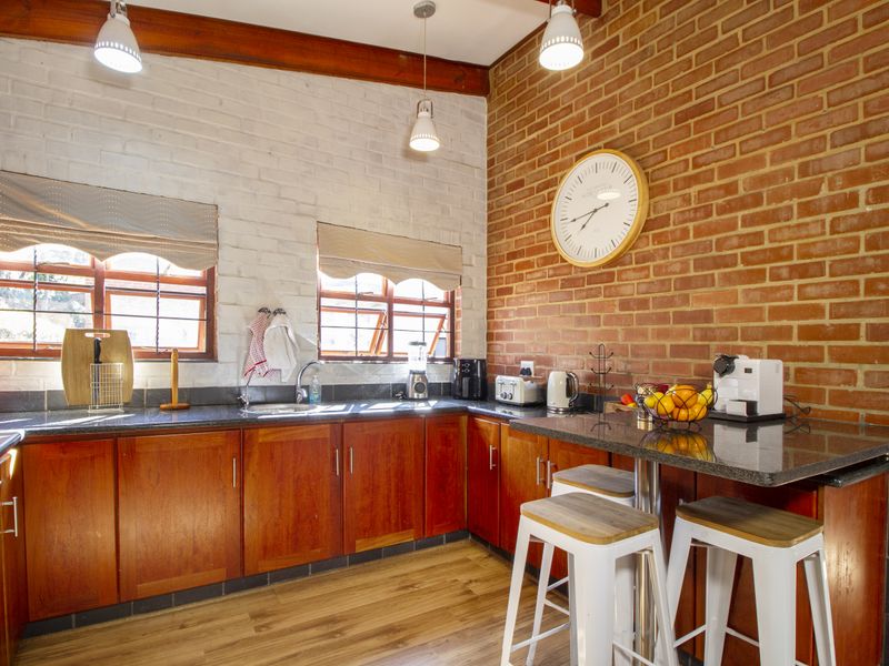 A warm kitchen featuring exposed brick walls, timber ceiling beams, granite countertops, and wooden cabinetry, creating a rustic and inviting culinary space.