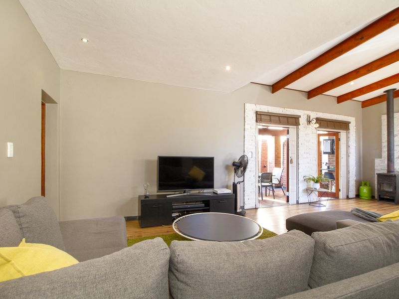 Spacious living room featuring exposed timber ceiling beams, a cozy wood-burning fireplace with a white brick surround, and direct access to the patio.