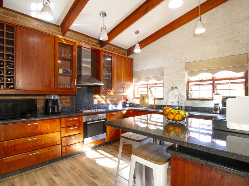 A warm, rustic-style kitchen featuring rich wooden cabinetry, granite countertops, exposed ceiling beams, and a brick feature wall with integrated appliances.