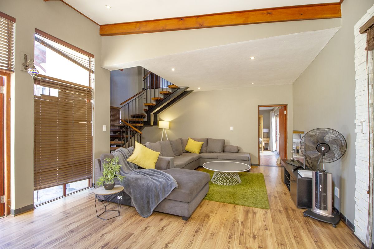Spacious living room featuring laminate flooring, an exposed timber ceiling beam, a stone feature wall, and an open staircase with metal railings.