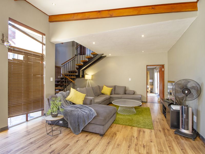 Spacious living room featuring laminate flooring, an exposed timber ceiling beam, a stone feature wall, and an open staircase with metal railings.