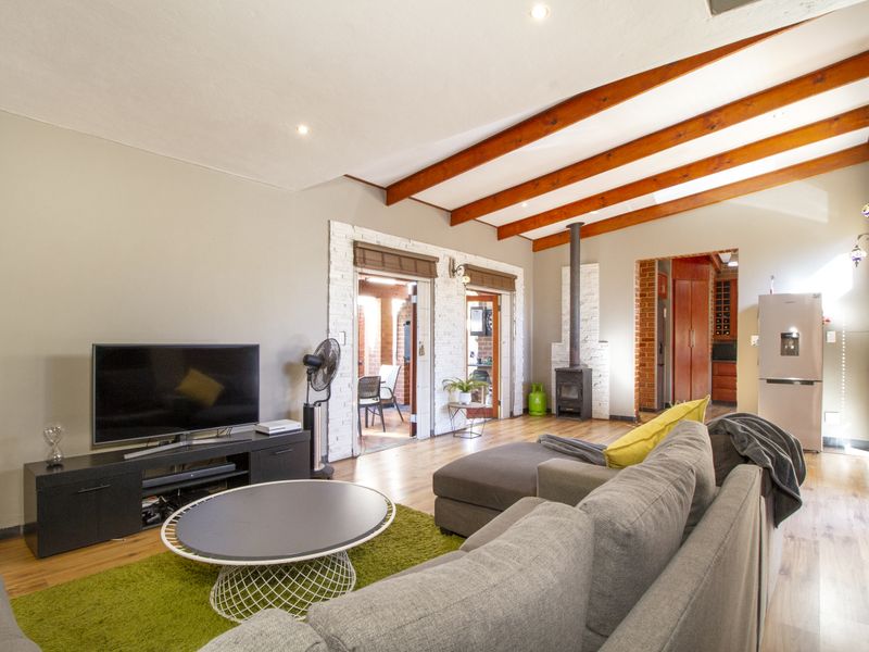 Spacious living area featuring exposed timber ceiling beams, a wood-burning fireplace, and laminate flooring, with direct access to an outdoor patio area.