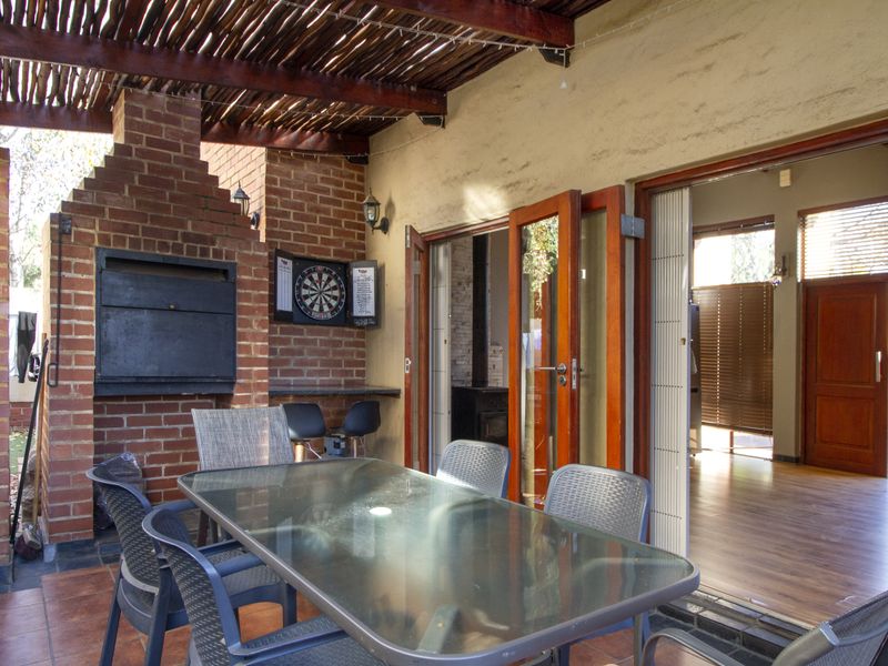 Covered patio area featuring a built-in brick braai, timber pergola roof, and wooden folding doors providing seamless access to the interior living space.