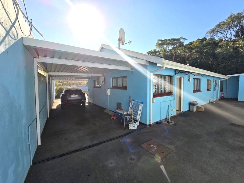 Rear exterior view of the house featuring a covered carport, asphalt driveway, and security bars on the windows.