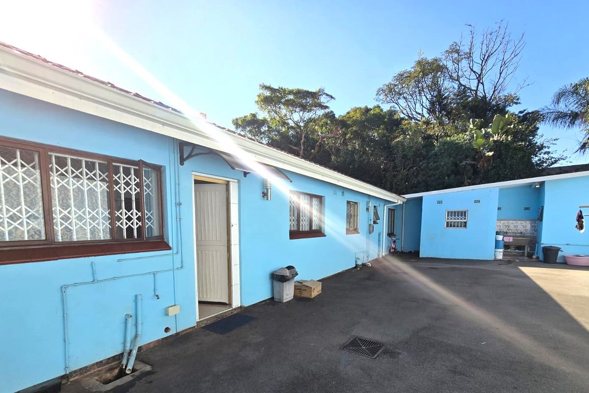 Rear exterior view of the property featuring paved courtyard area, security gates on windows, and blue painted exterior walls.