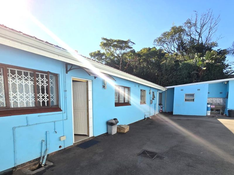Rear exterior view of the property featuring paved courtyard area, security gates on windows, and blue painted exterior walls.