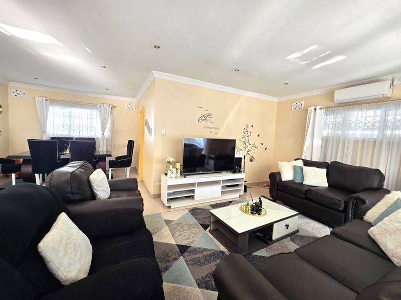 Spacious open-plan living and dining area featuring tiled flooring, recessed downlighting, crown molding, and a wall-mounted split-system air conditioner.