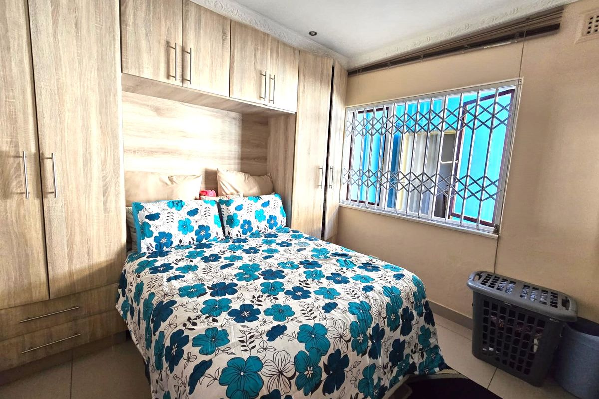A bedroom featuring built-in wooden cupboards, tiled flooring, and a window fitted with a security gate.
