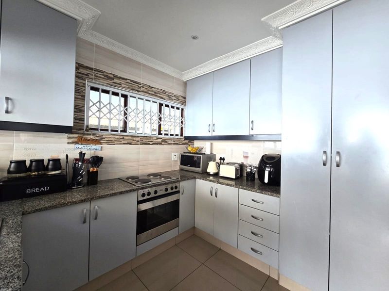 A functional kitchen featuring light grey built-in cabinetry, granite countertops, a built-in oven and hob, and a tiled backsplash with a window security gate.