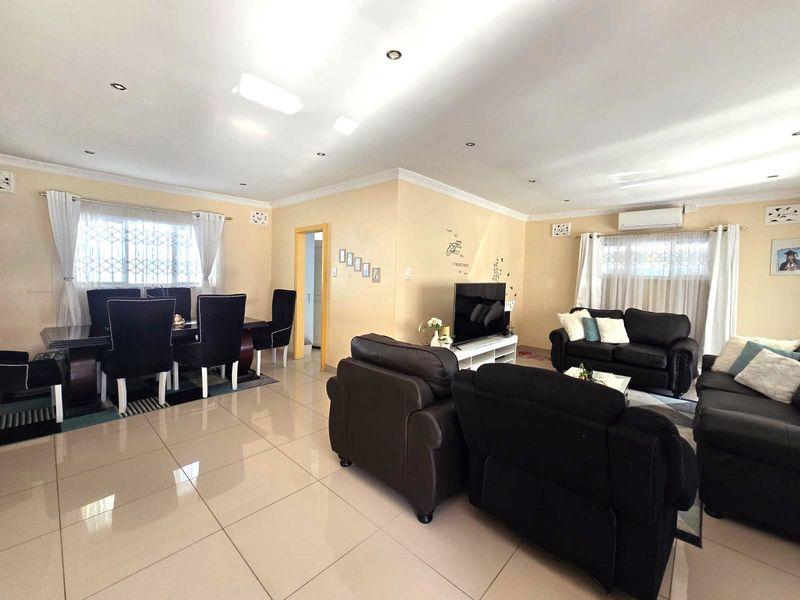 Spacious open-plan living and dining area featuring neutral tiled flooring, recessed lighting, and a wall-mounted air conditioning unit.