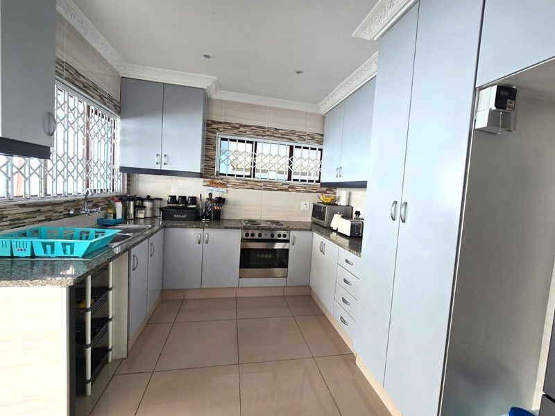 A functional kitchen featuring light-toned built-in cabinetry, granite countertops, stainless steel oven and hob, tiled flooring, and secure window bars.
