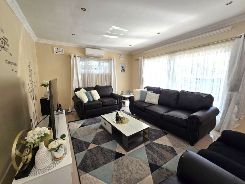 A well-maintained living room featuring tiled flooring, recessed downlighting, decorative ceiling cornices, and a wall-mounted split-system air conditioner.