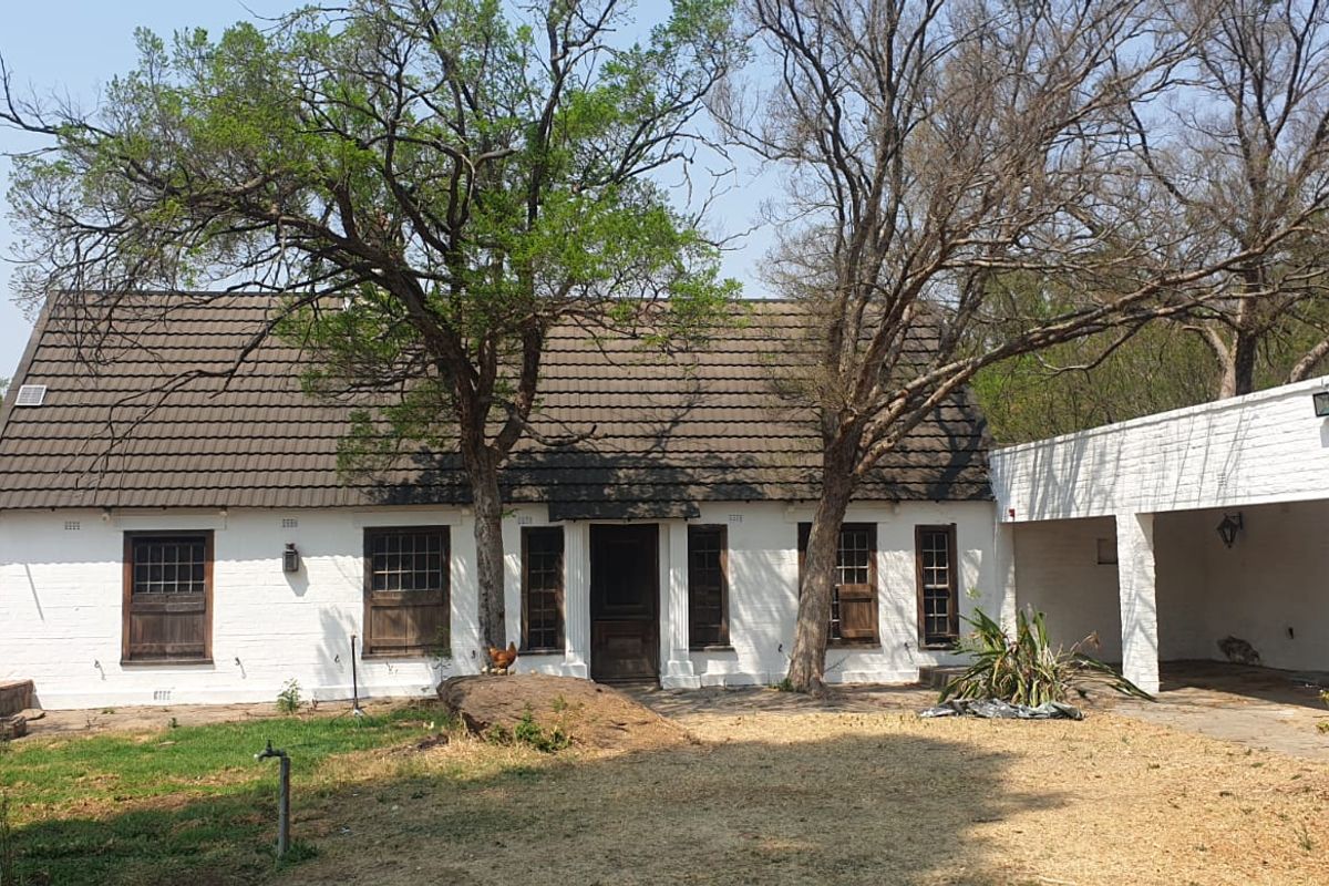 Rear view of a traditional farm-style residence featuring a tiled roof, white brick facade, and an attached covered patio area.