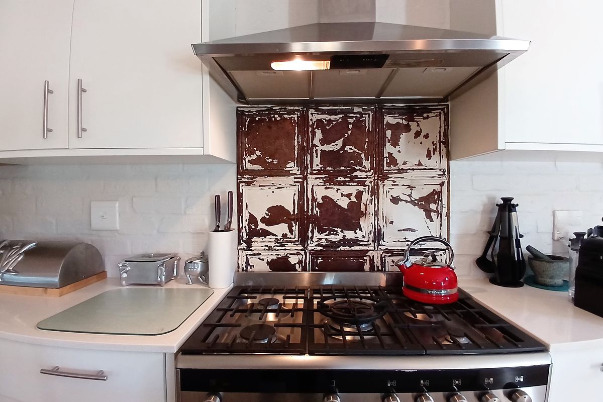 A kitchen cooking area featuring a gas stove, stainless steel extractor fan, white cabinetry, and a unique distressed metal backsplash.