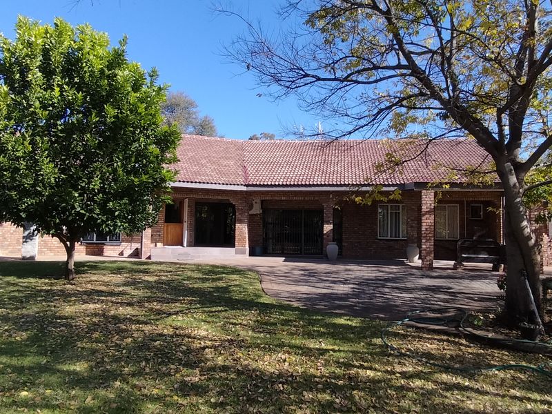 Rear view of a brick house featuring a tiled roof, a covered patio area, and a spacious garden with mature trees.