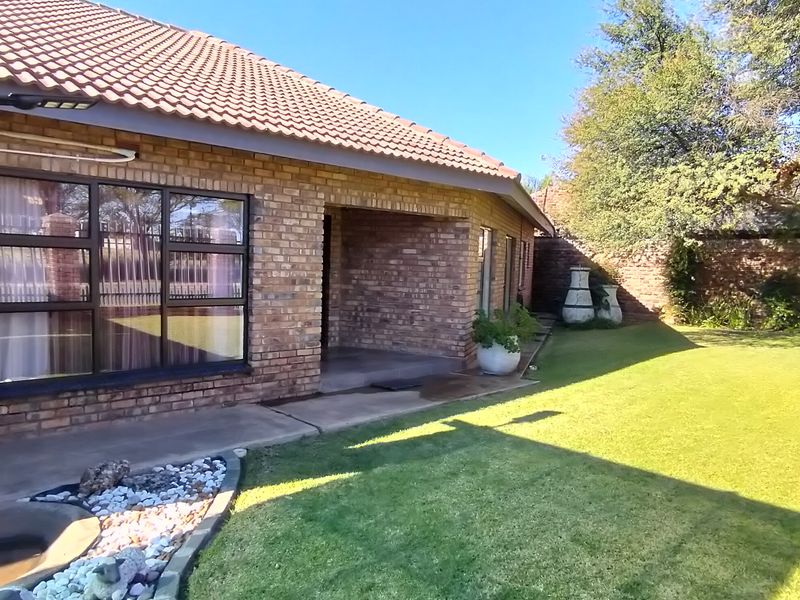 A well-maintained rear exterior view of a face-brick house featuring a tiled roof, aluminum windows, and a spacious landscaped garden.