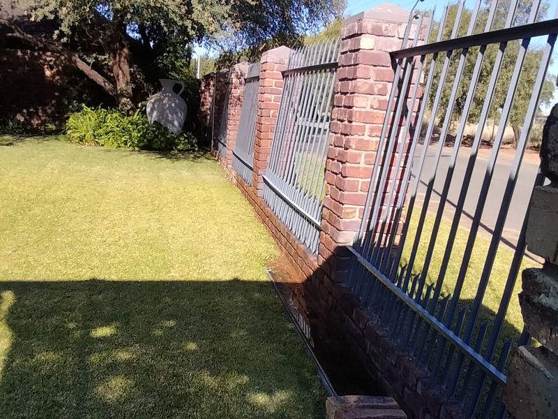 A well-maintained garden area featuring a brick boundary wall with integrated metal security fencing and electric wiring, adjacent to a neat lawn.
