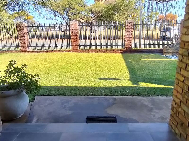 A covered patio area featuring brick pillars and tiled flooring, overlooking a private lawn and secure perimeter fencing.