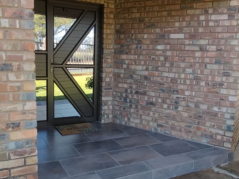Covered entrance porch featuring face-brick walls, tiled flooring, and a modern security gate, providing a secure and welcoming entry point to the home.