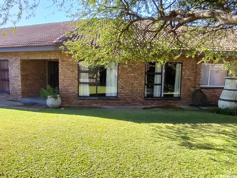 Rear view of a single-story brick house featuring a tiled roof, aluminium window frames with security bars, and a well-maintained lawn.
